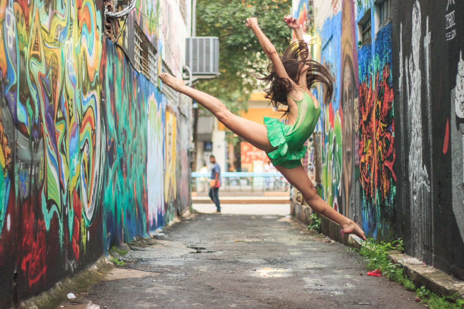 woman-in-a- green-dress-leaps-in-a-vibrant-graffiti-filled-alley